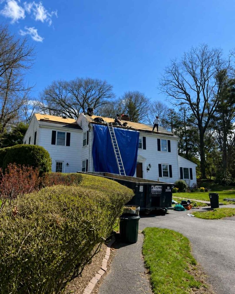 Roofing crew installing asphalt shingles on white residential home
